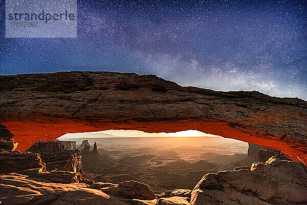 Eine seltene Aufnahme der Milchstraße und des aufgehenden Mondes  die die Wüstenlandschaft unterhalb des Mesa Arch beleuchten  Canyonlands National Park; Utah  Vereinigte Staaten von Amerika