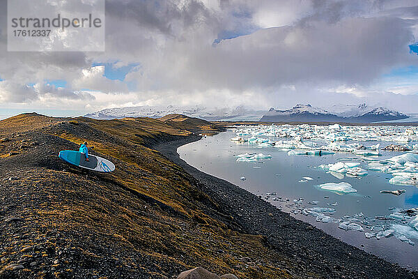 Ein Mann  der mit einem Paddleboard zur Gletscherlagune Jokulsarlon hinunterfährt.