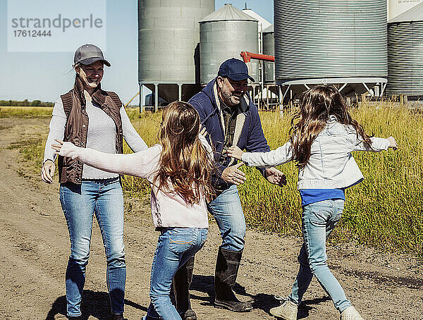 Zwei junge Mädchen  die ihren Eltern auf der Familienfarm entgegenlaufen  mit Getreidespeichern im Hintergrund; Alcomdale  Alberta  Kanada