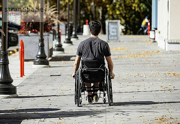 Junger querschnittsgelähmter Mann in seinem Rollstuhl  der an einem schönen Herbsttag einen städtischen Gehweg hinunterfährt; Edmonton  Alberta  Kanada
