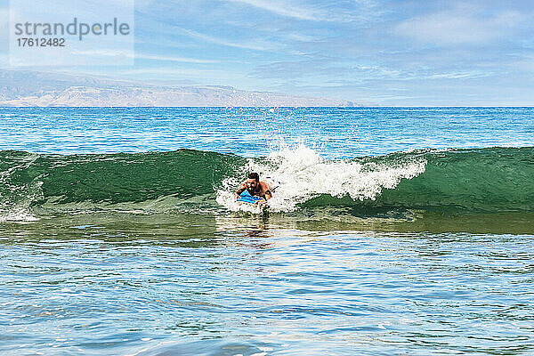 Ein Mann reitet auf einer Welle auf einem Bodyboard gegen das Ufer des D. T. Fleming Beach mit der Insel Molokai im Hintergrund; Kapalua  Maui  Hawaii  Vereinigte Staaten von Amerika