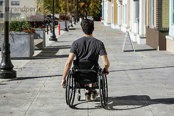Junger querschnittsgelähmter Mann in seinem Rollstuhl  der an einem schönen Herbsttag einen städtischen Gehweg hinunterfährt; Edmonton  Alberta  Kanada