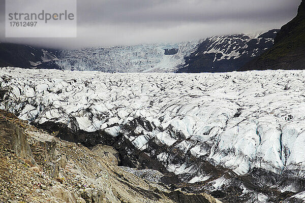 Entfernte Wanderer werden von einem massiven isländischen Gletscher in den Schatten gestellt; Svinafellsjokull-Gletscher  Skaftafell-Nationalpark  Island.