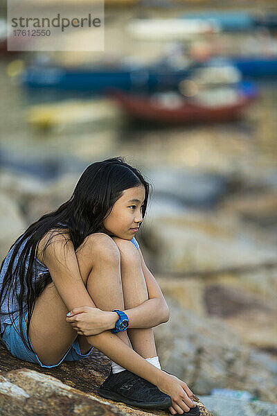 Junges Mädchen sitzt auf einem Felsen am Hafenufer; Stanley  Hongkong  China