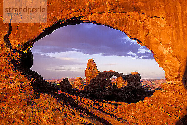 Blick durch den augenförmigen Window Arch auf den Turret Arch  wobei das Sonnenlicht einen roten Schimmer auf die Sandsteinfelsen im Arches National Park wirft; Utah  Vereinigte Staaten von Amerika