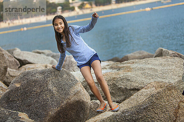 Junges Mädchen schaut in die Kamera  während es auf große Felsen in der Repulse Bay klettert; Hongkong  China