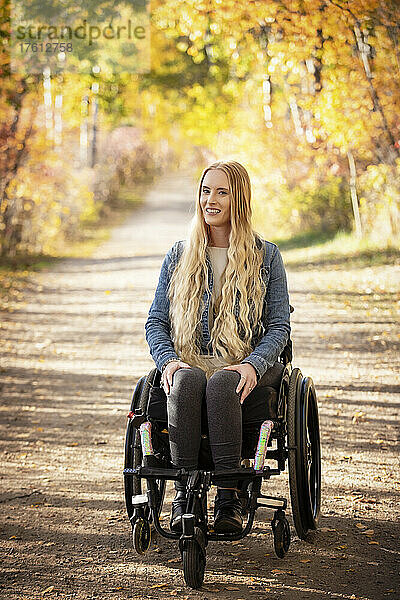 Junge querschnittsgelähmte Frau in ihrem Rollstuhl  die an einem schönen Herbsttag einen Weg in einem Park hinunterfährt; Edmonton  Alberta  Kanada