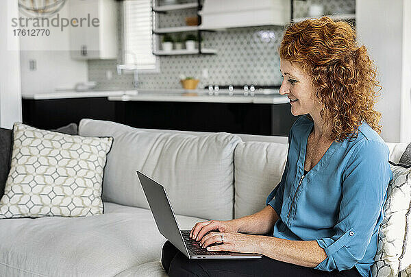 Frau sitzt zu Hause auf einer Couch und benutzt ihren Laptop; Edmonton  Alberta  Kanada