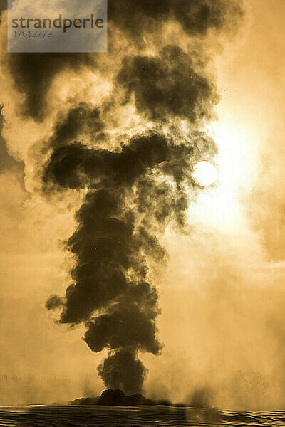 Silhouette der thermischen Dampfwolken  die aus dem Old Faithful ausbrechen  während der Himmel im goldenen Licht des Sonnenaufgangs im Upper Geyser Basin erleuchtet wird; Yellowstone National Park  Vereinigte Staaten von Amerika