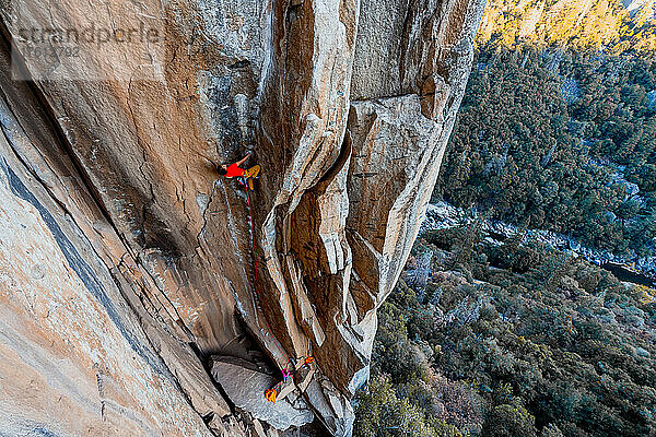 Ein Mann klettert in einem technischen Granit-Risssystem hoch über einem Tal.