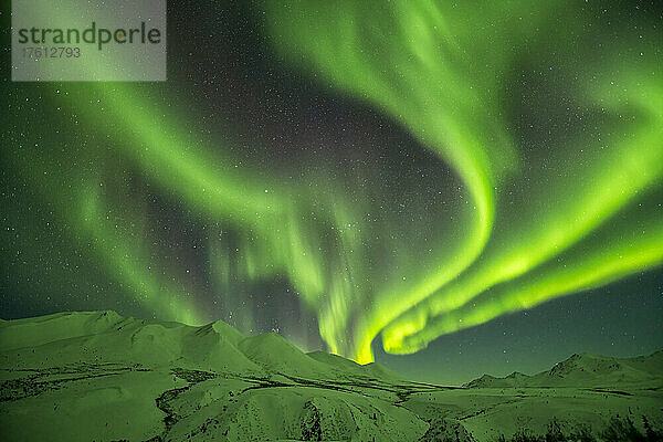 Aurora borealis (oder Nordlicht) am Sternenhimmel über den schneebedeckten Bergen entlang des Dempster Highway im Winter; Yukon  Kanada