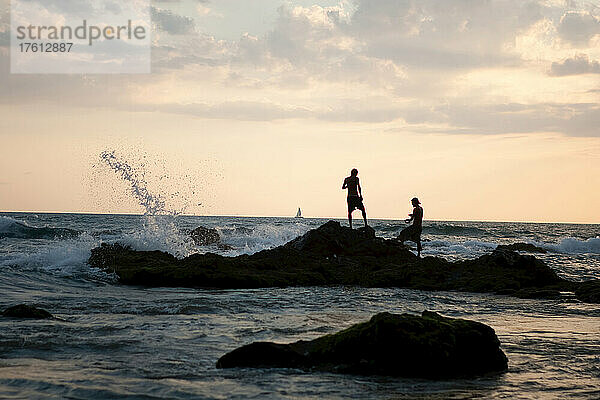 Männer beim Fischen vor den Felsen bei Sonnenuntergang.