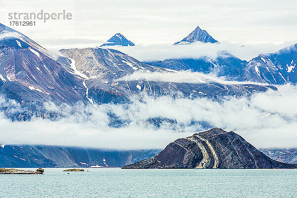 Eine Insel aus gefaltetem Gestein liegt am Fuße einer Bergkette.