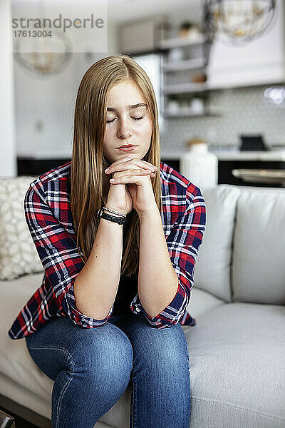 Teenager-Mädchen sitzt zu Hause auf einer Couch und verbringt Zeit im Gebet; Edmonton  Alberta  Kanada