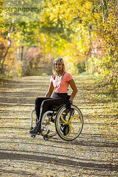 Porträt einer jungen querschnittsgelähmten Frau in ihrem Rollstuhl auf einem Weg in einem Park an einem schönen Herbsttag; Edmonton  Alberta  Kanada