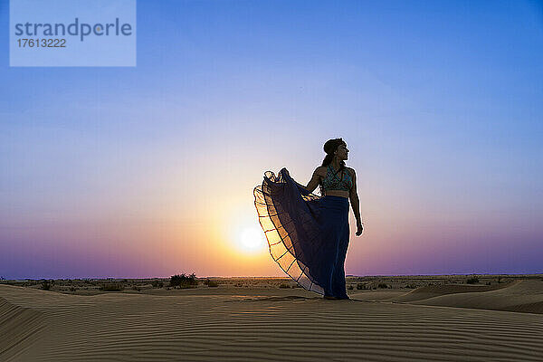 Frau mit langem Rock im Gegenlicht des Sonnenuntergangs im Wüstensand; Abu Dhabi  Vereinigte Arabische Emirate
