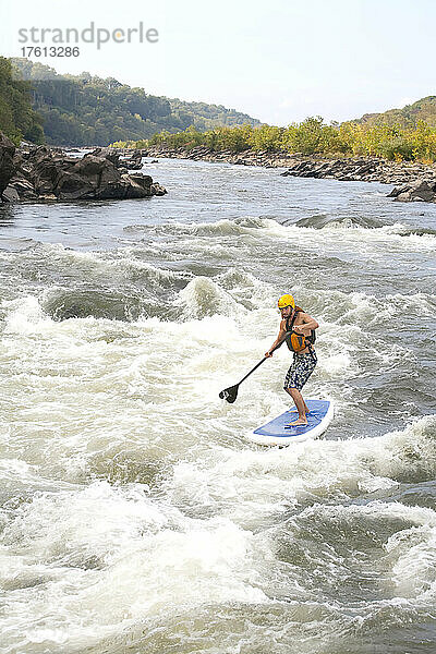 Ein Mann auf einem Stand Up Paddle Board fährt auf dem Potomac River durch Stromschnellen; Bethesda  Maryland.