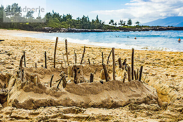 Eine Sandburg mit Stöcken an den Rändern am Ufer des D. T. Fleming Park  mit Schwimmern im Wasser und der Insel Molokai im Hintergrund; Kapalua  Maui  Hawaii  Vereinigte Staaten von Amerika