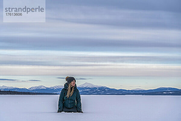 Frau kniet im tiefen Schnee und betrachtet die Landschaft am zugefrorenen Tagish Lake; Tagi; Tagish  Yukon  Kanada