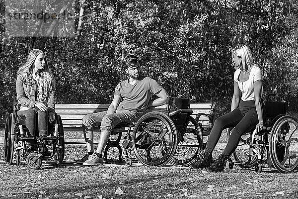 Schwarz-Weiß-Bild einer Gruppe von drei jungen Querschnittsgelähmten in ihren Rollstühlen  die an einem schönen sonnigen Tag gemeinsam einen Park besuchen; Edmonton  Alberta  Kanada