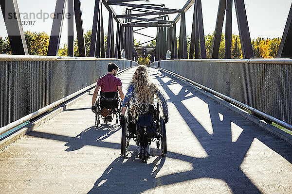 Junger querschnittsgelähmter Mann und Frau  die an einem schönen Herbsttag gemeinsam in ihren Rollstühlen über eine Brücke fahren; Edmonton  Alberta  Kanada