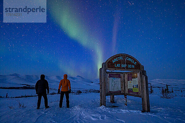 Blick von hinten auf zwei Personen  die das Polarlicht über dem Dempster Highway am Nachthimmel an der Grenze zum Polarkreis beobachten; Yukon  Kanada