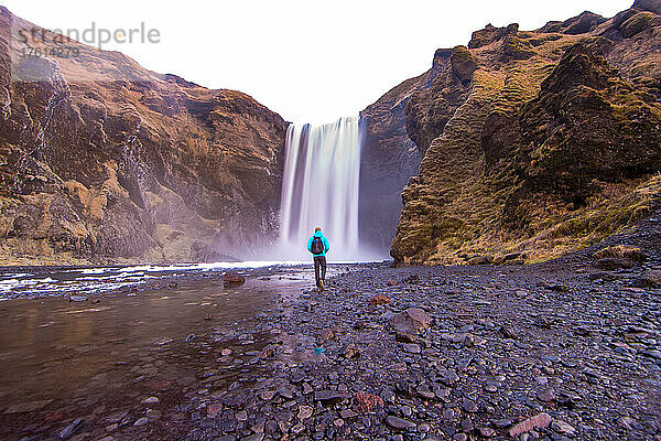 Ein Mann geht zum Skogafoss-Wasserfall in Island.