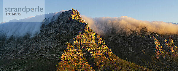 Blick auf den sonnenbeschienenen Tafelberg vom Lion's Head mit einer Wolkenformation  die einen Tischtuch-Effekt über den Berggipfeln erzeugt; Kapstadt  Westkap-Provinz  Südafrika
