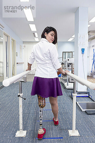 Junge Frau mit Beinprothese in Therapie  geht mit Handläufen; Bangkok  Thailand