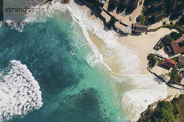 Blick von oben auf die Brandung  die auf den Strand von Nusa Lembongan rollt  mit Gebäuden am Rande des türkisfarbenen Wassers vor der Küste Balis; Nusa-Inseln  Klungkung Regency  Ost-Bali  Indonesien