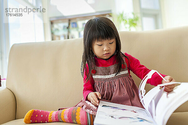 Junges Mädchen sitzt auf einer Couch und liest ein Märchenbuch; Hongkong  China