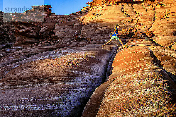 Ein Mädchen springt über Risse in einer roten Sandsteinformation auf der Halbinsel Baja bei Puerto Gato.