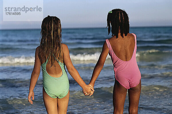 Rückenansicht von zwei Mädchen in Badekleidung  die am Strand von Süd-Andros  Bahamas  Händchen halten