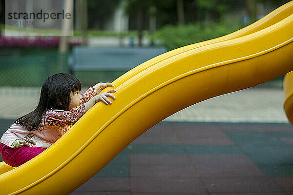 Junges Mädchen spielt auf einer gelben Rutsche auf einem Spielplatz; Hongkong  China