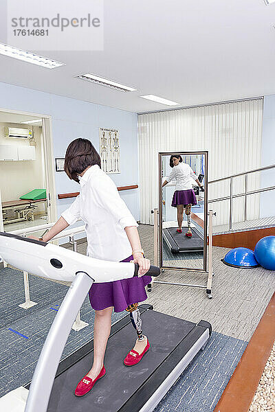 Junge Frau mit Beinprothese in Therapie  die auf einem Laufband läuft und dabei ihr Spiegelbild betrachtet; Bangkok  Thailand