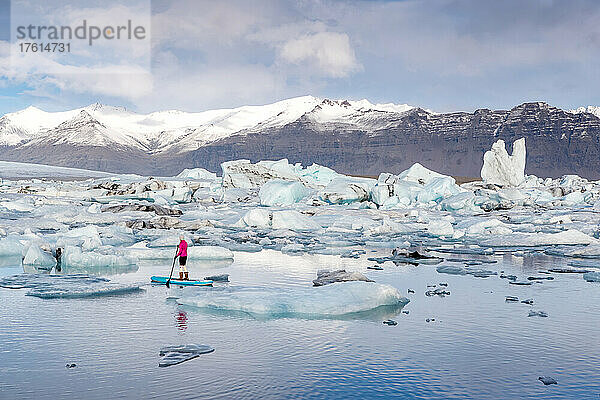 Eine Frau auf einem aufblasbaren Paddleboard paddelt auf der Lagune des Jokulsarlon-Gletschers.
