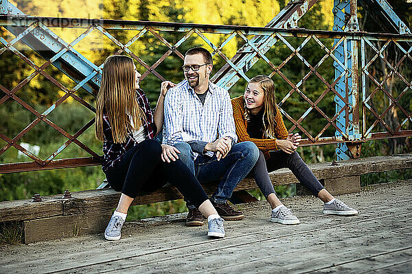 Vater mit zwei Töchtern im Teenageralter sitzen auf einer Brücke und unterhalten sich in einem Stadtpark im Herbst; Edmonton  Alberta  Kanada