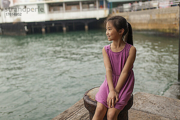 Mädchen sitzt auf dem Pier im Victoria Harbour und blickt auf das Wasser; Hongkong  China