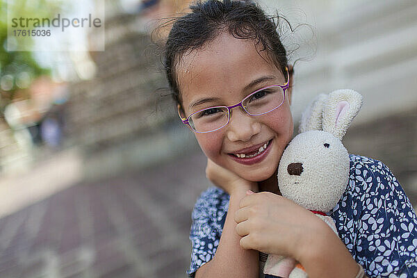 Porträt eines jungen Mädchens  das eine Brille trägt und sein Stofftierkaninchen im Arm hält; Bangkok  Thailand