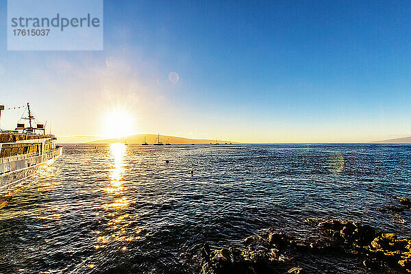 Sonnenlicht  das sich bei Sonnenuntergang auf dem Wasser spiegelt  und vor der Küste vertäute Segelboote mit Blick auf die Insel Lanai von einem Strand in Lahaina; Lahaina  Maui  Hawaii  Vereinigte Staaten von Amerika