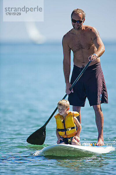 Ein Mann paddelt mit seinem kleinen Sohn auf einem Stand Up Paddleboard in den Wellen.