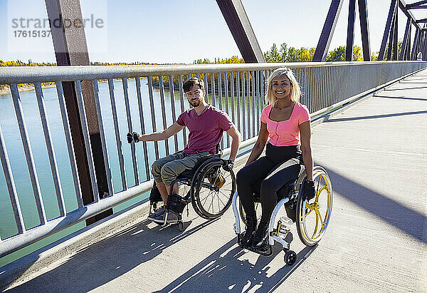 Zwei junge querschnittsgelähmte Freunde verbringen Zeit miteinander  indem sie sich an einem schönen Tag in einem Stadtpark in ihren Rollstühlen über eine Parkbrücke bewegen; Edmonton  Alberta  Kanada