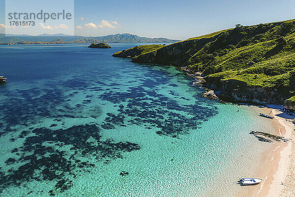 Luftaufnahme von Motorbooten am Strand eines rosa Sandstrandes und Menschen  die das Meer entlang der Küste der Insel Padar im Komodo-Nationalpark genießen; East Nusa Tenggara  Lesser Sunda Islands  Indonesien