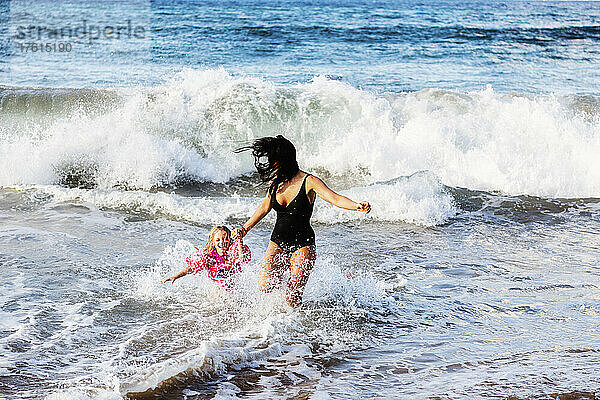 Junge Mutter spielt mit ihrer Tochter und läuft vor den Wellen am D. T. Fleming Beach weg; Kapalua  Maui  Hawaii  Vereinigte Staaten von Amerika