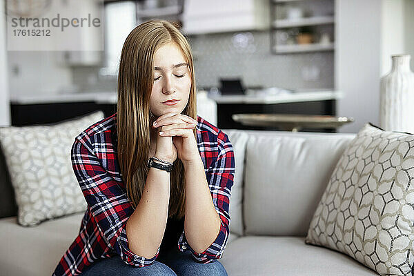 Teenager-Mädchen sitzt zu Hause auf einer Couch und verbringt Zeit im Gebet; Edmonton  Alberta  Kanada