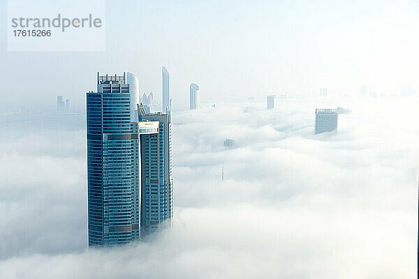 Überblick über Abu Dhabi City mit Blick auf die Nation Towers und andere Hochhäuser  einschließlich der beiden Türme des World Trade Center Abu Dhabi Complex in der Ferne  die durch die sonnenbeschienenen Wolken und den Nebel auftauchen; Abu Dhabi  Vereinigte Arabische Emirate