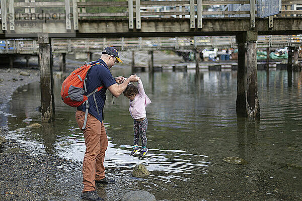 Vater und kleine Tochter spielen am Rande eines Strandes am Hafen von Horseshoe Bay in BC  Kanada; West Vancouver  British Columbia  Kanada