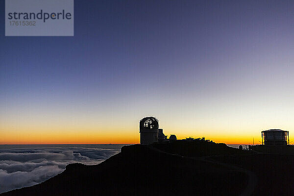 Gebäude des Haleakala-Observatoriums über den Wolken entlang der Spitze einer silhouettierten Landschaft mit einem goldenen Sonnenuntergang; Maui  Hawaii  Vereinigte Staaten von Amerika