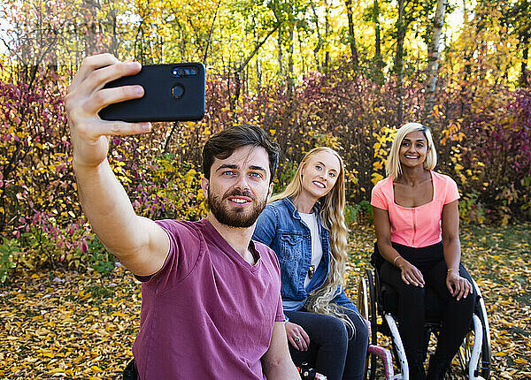 Junger querschnittsgelähmter Mann und Frau in ihren Rollstühlen  die an einem schönen Herbsttag in einem Park ein Selbstporträt mit einem Smartphone aufnehmen; Edmonton  Alberta  Kanada