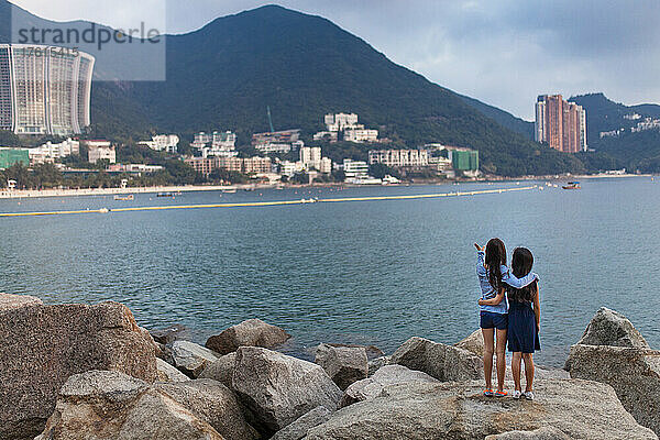 Junge Schwestern stehen in einer Umarmung und blicken auf die Repulse Bay in Hongkong; Hongkong  China